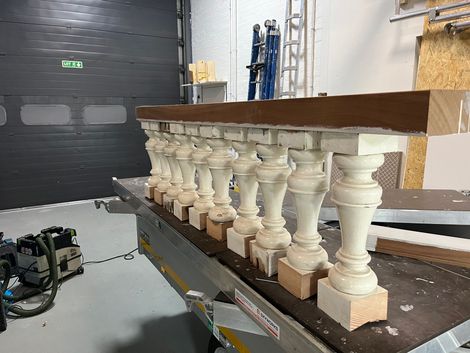 Houten balustrade in werkplaats, crèmekleurige spijlen, bruine bovenregel, op een werktafel, met gereedschap op de achtergrond.