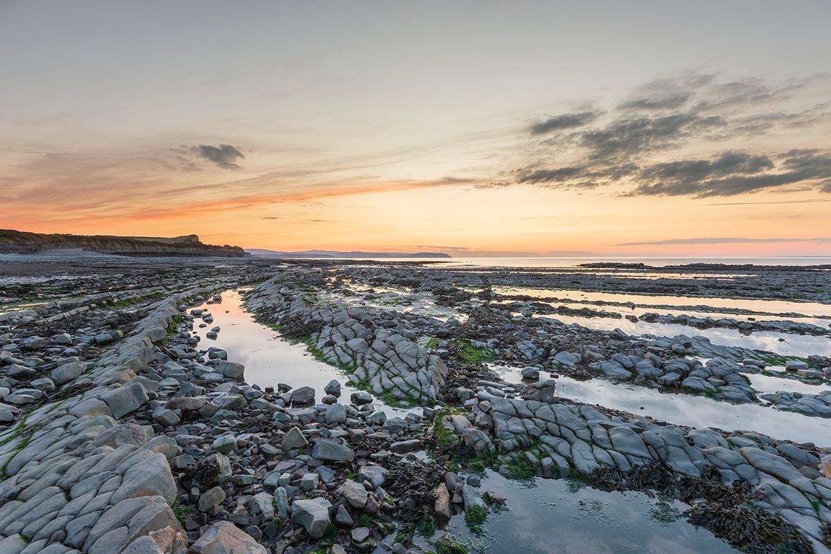 A sunset over a rocky beach with a stream running through it.