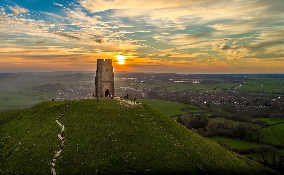 The sun is setting behind a castle on top of a hill.