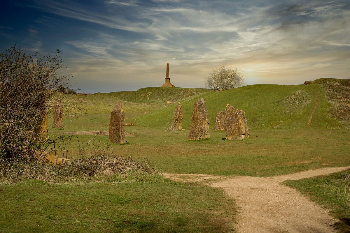 A dirt path going through a grassy field with a monument in the background.