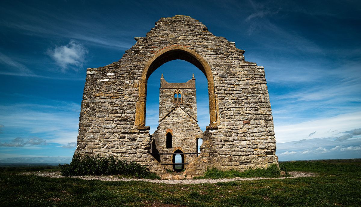 A large stone archway in the middle of a field with a blue sky in the background.