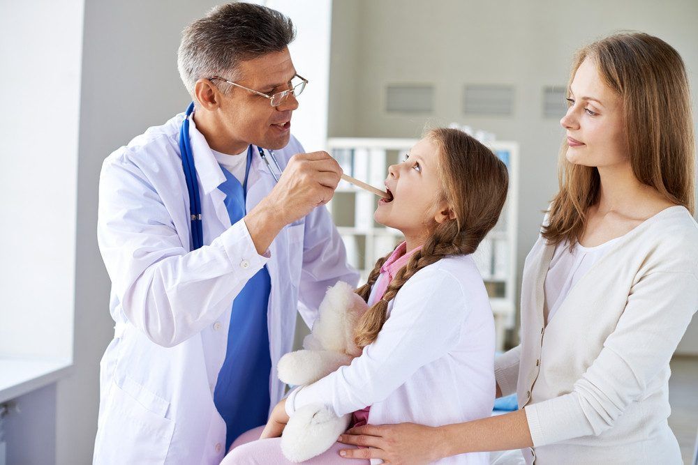 A doctor is looking into a girl's mouth.