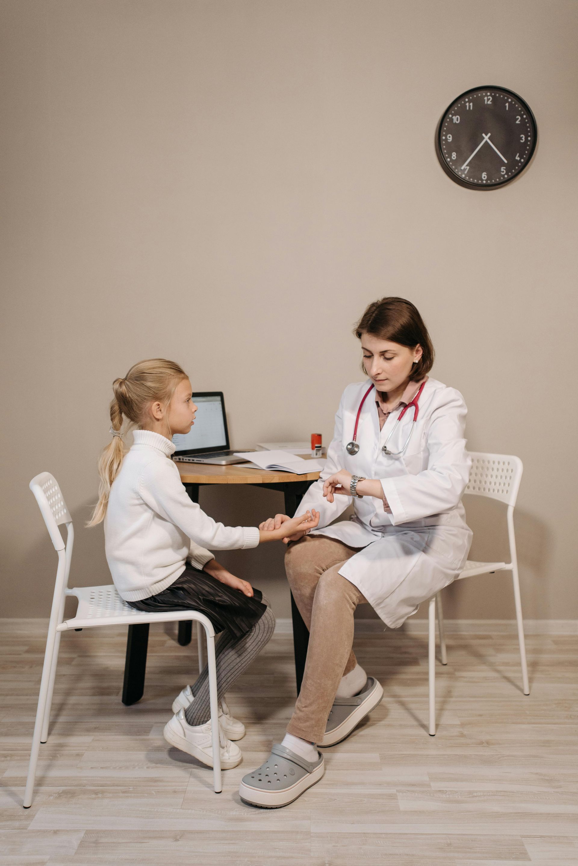 A doctor is sitting on a chair taking a girl's pulse.