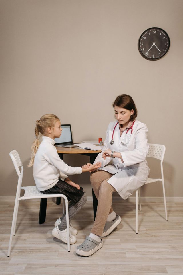 A doctor is sitting on a chair taking a girl's pulse.