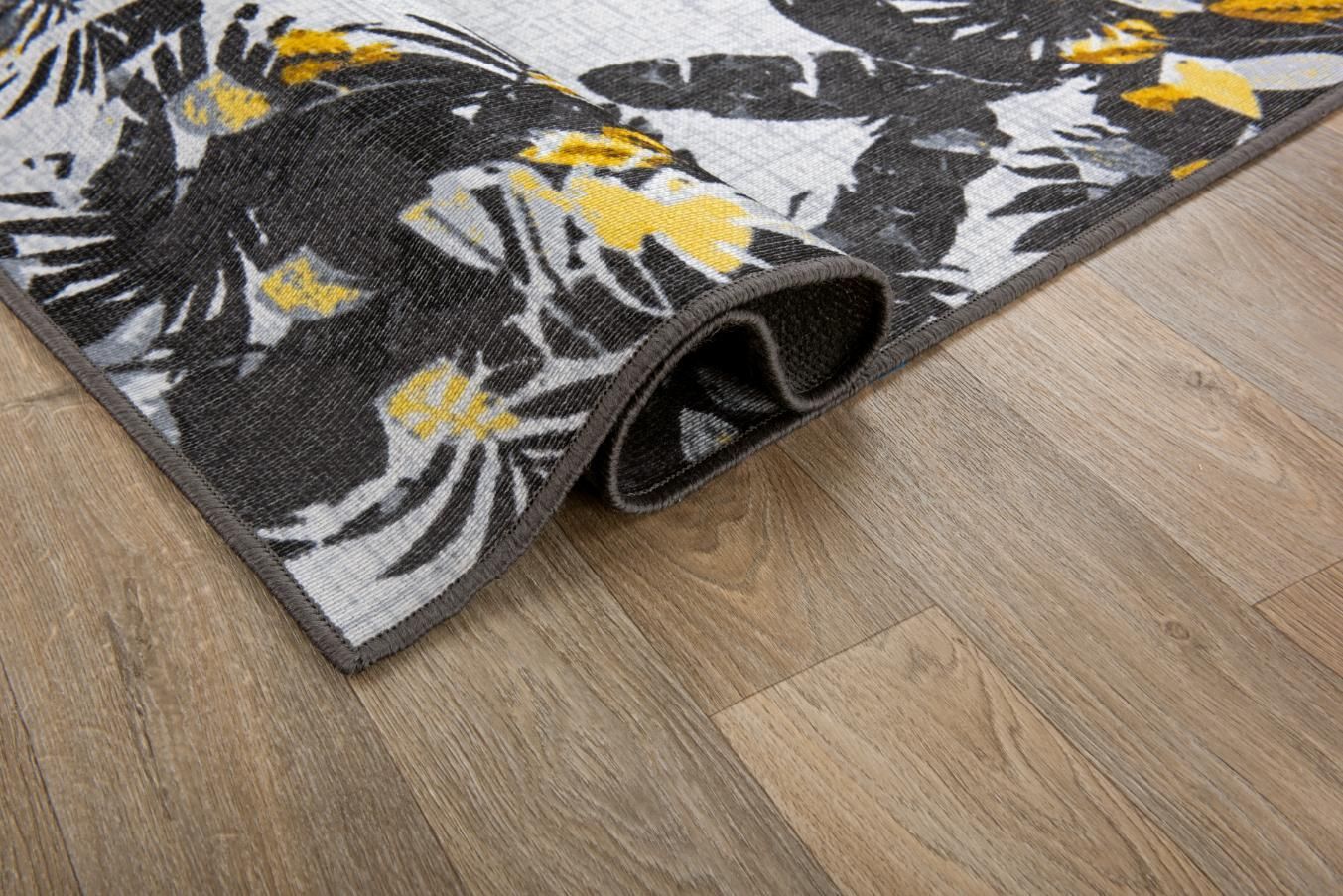 Folded black-and-white floral rug corner on a light wood floor