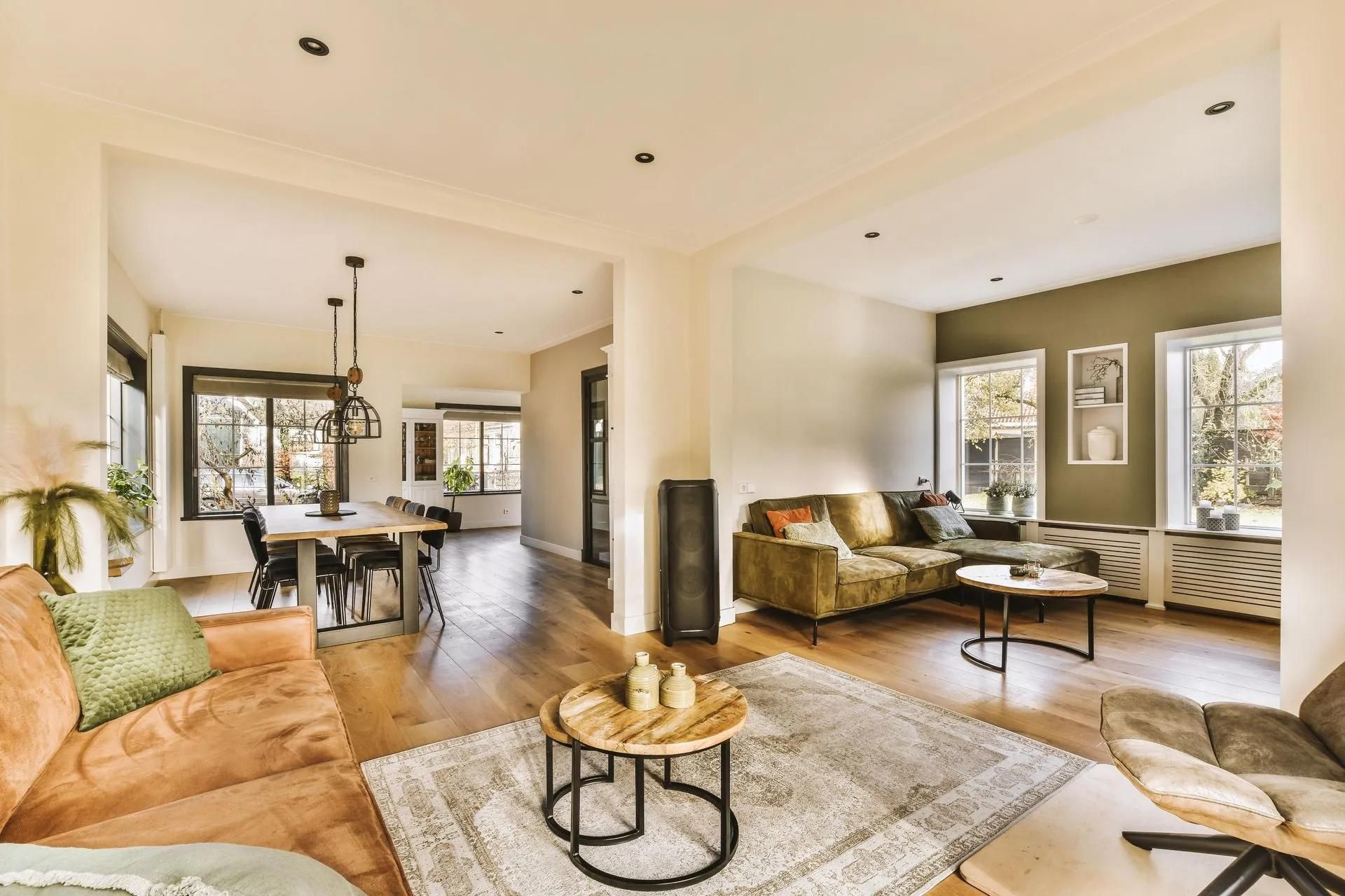 Bright open-plan living room with beige sofas, rug, coffee table, and dining area by large windows