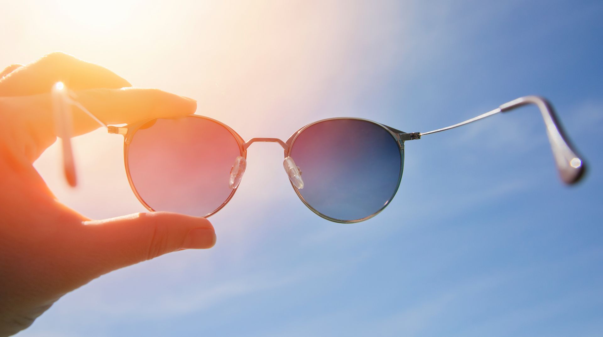 Round sunglasses held up against a bright blue sky with sunlight shining through Round sunglasses held up against a bright blue sky with sunlight shining through