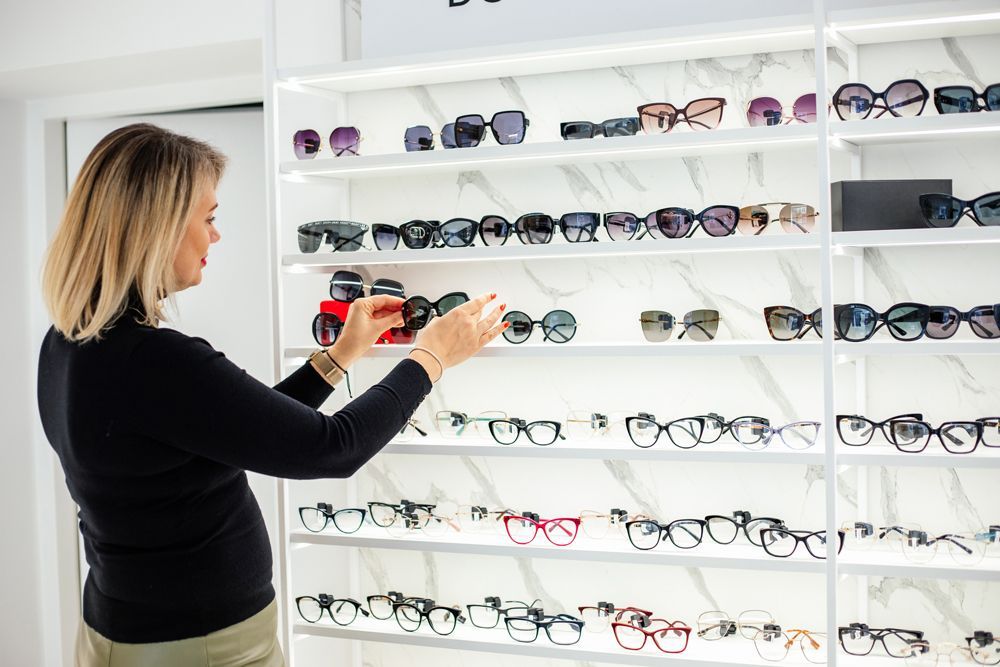Saleswoman reaching for stylish sunglasses on display in eyewear store, promoting sunglasses.