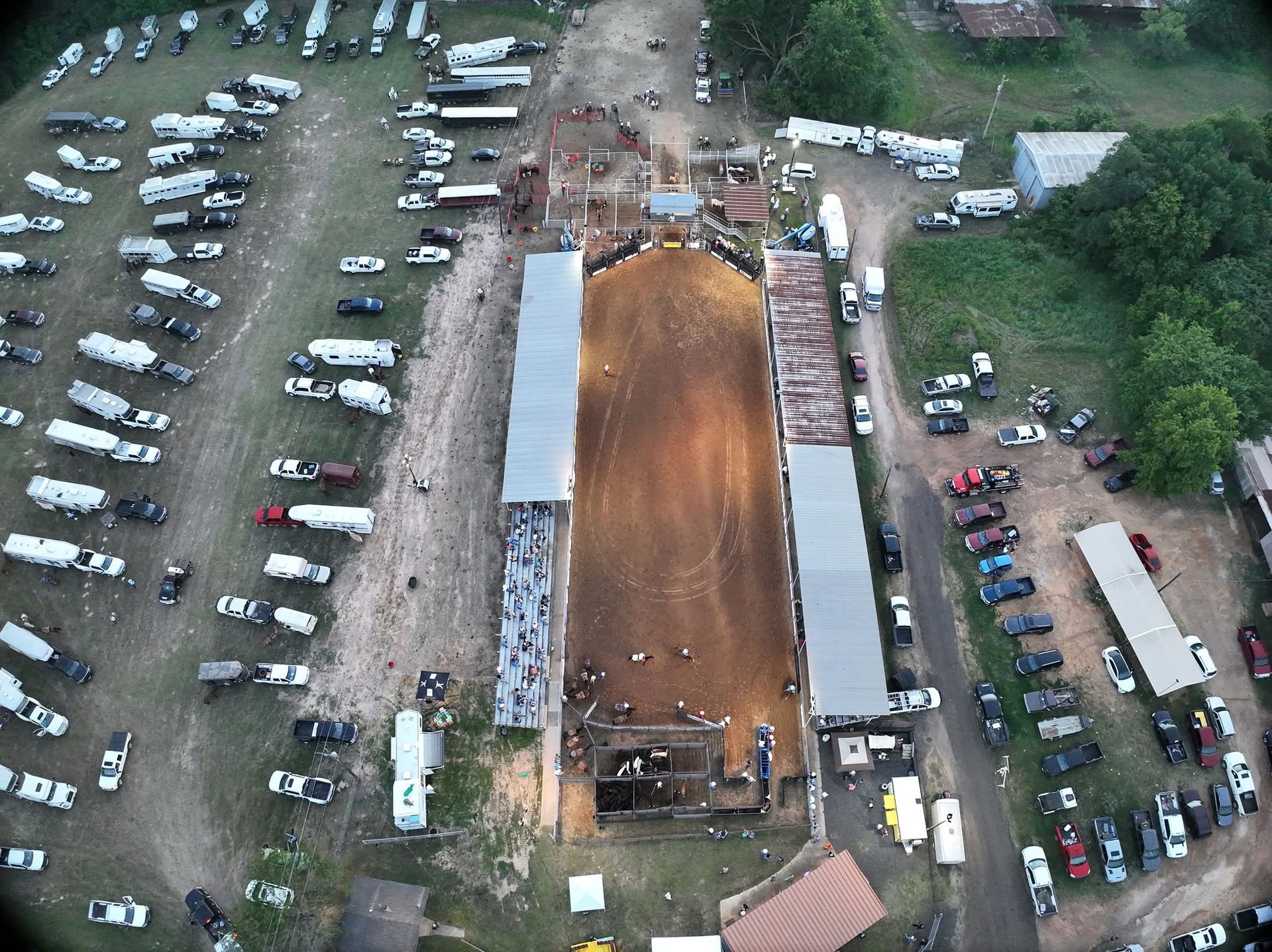 Aerial view of a rodeo arena in daylight with trucks and trailers parked around it