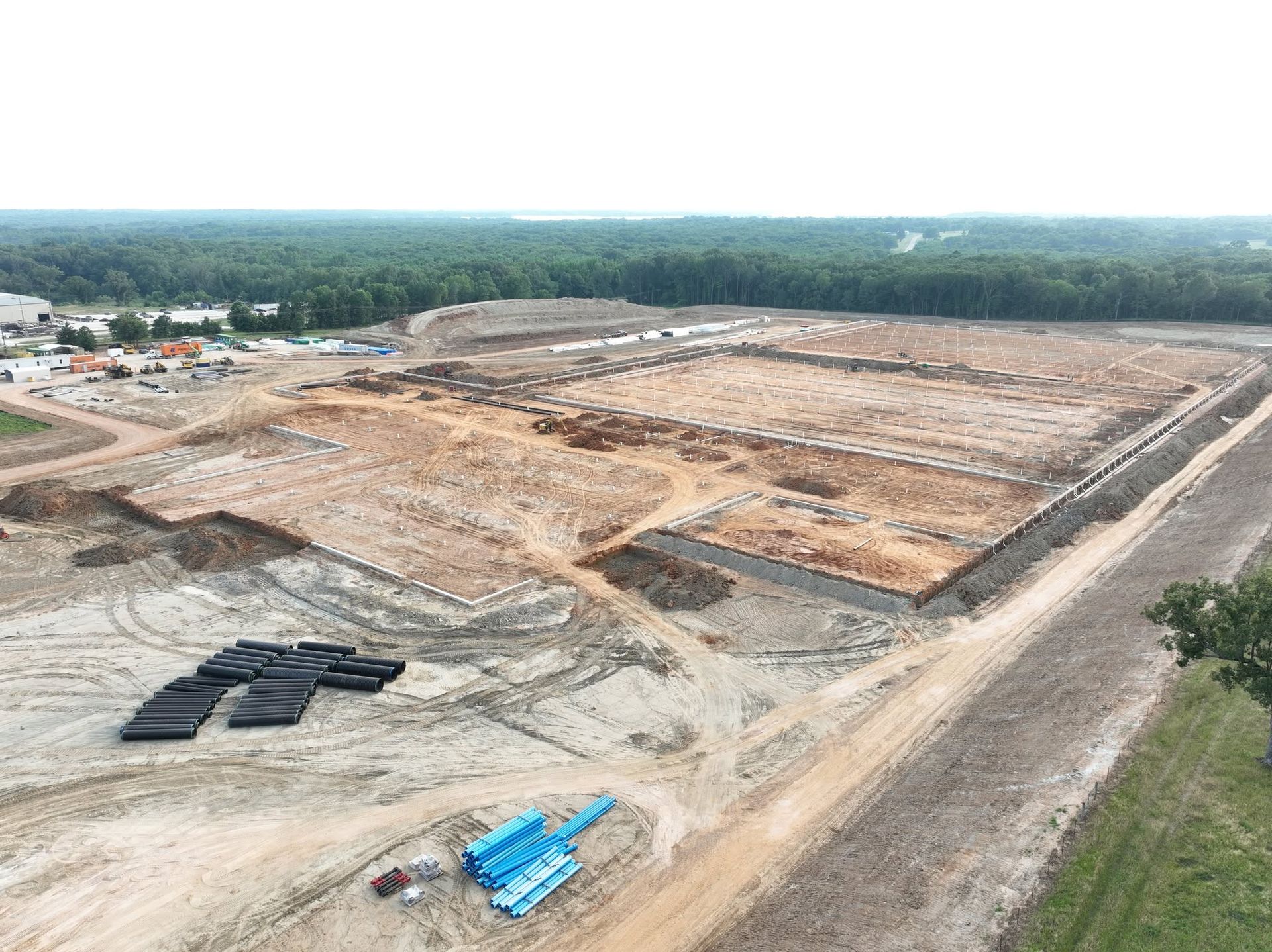 Wide aerial view of a large earthwork site with cut benches in red clay