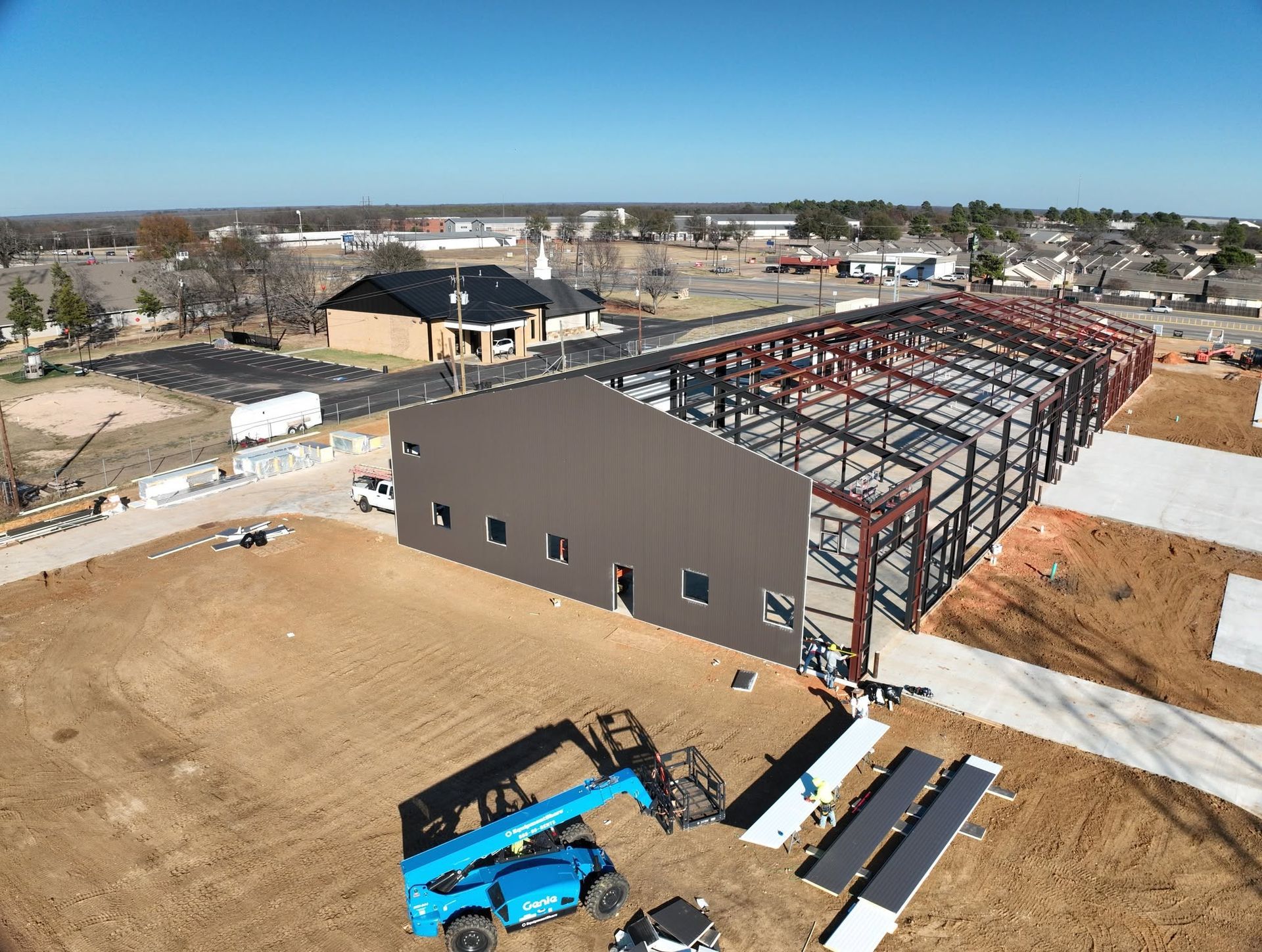 Aerial view of a steel-framed commercial building being clad, with a lift on site
