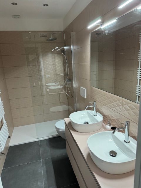 Moderne badkamer met dubbele wastafel, grote spiegel en betegelde douche.