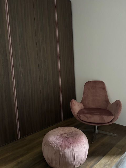 Roze stoel en voetenbank in een moderne kamer naast een donkerhouten kledingkast.