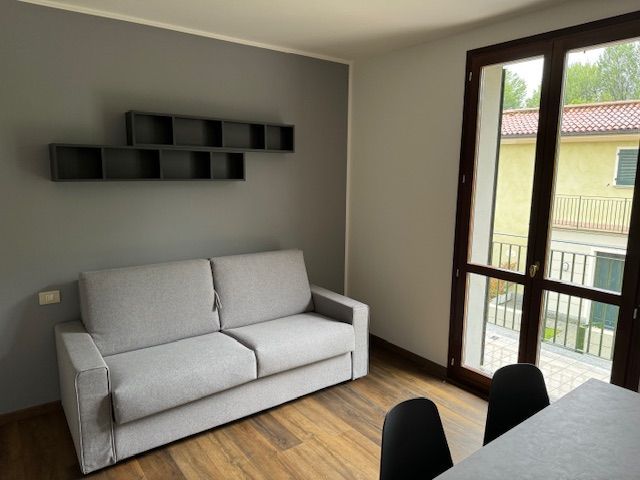 Woonkamer met grijze bank, zwevende planken en een glazen schuifdeur.