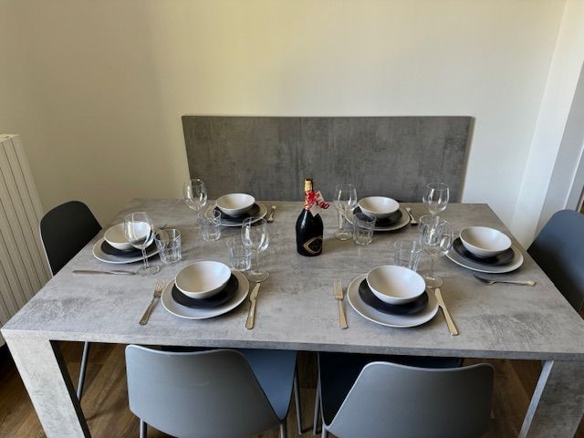Dek de eettafel voor zes personen met borden, kommen, glazen en een fles in het midden.