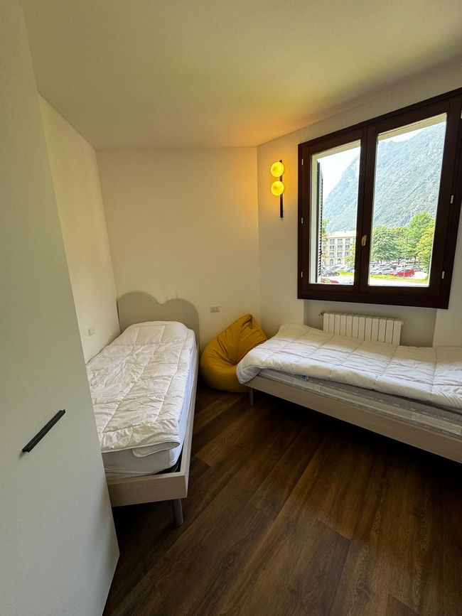 Kleine slaapkamer met twee eenpersoonsbedden, gele kussens en een raam met uitzicht op de bergen.