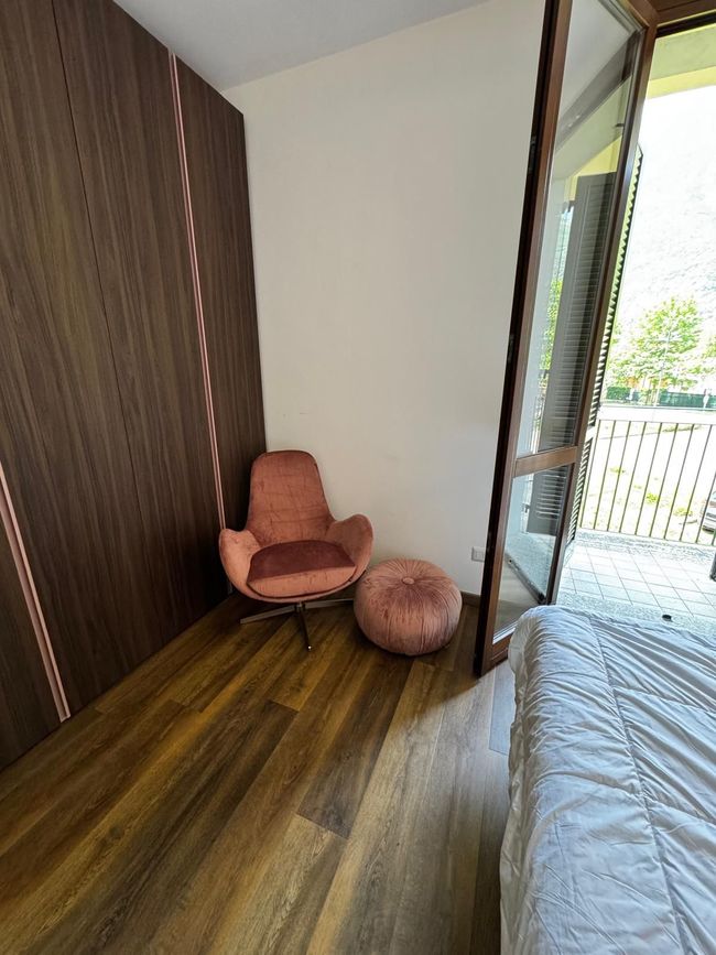 Moderne hoek met roze stoel en voetenbank in een kamer met houten lambrisering, grenzend aan een open balkondeur.