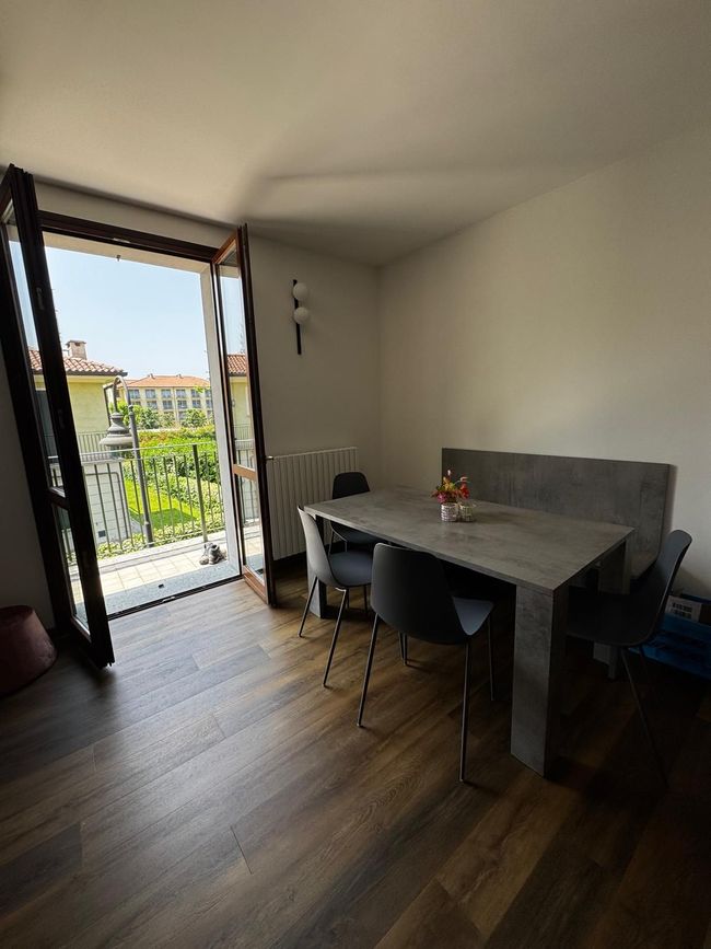 Moderne eetkamer met openslaande balkondeuren, grijze tafel, zwarte stoelen en uitzicht op de stad.