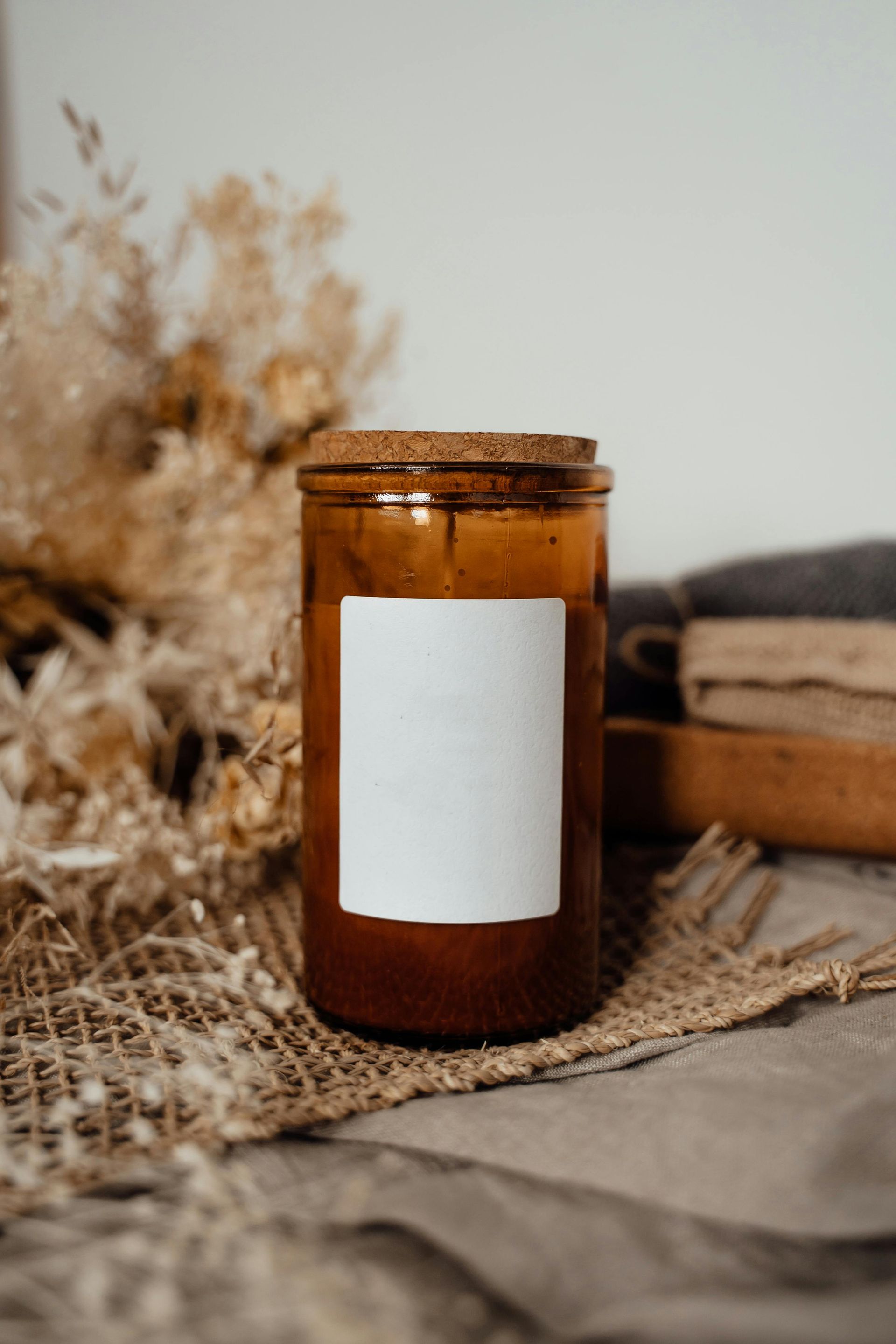 A candle in a brown glass jar with a blank white label.