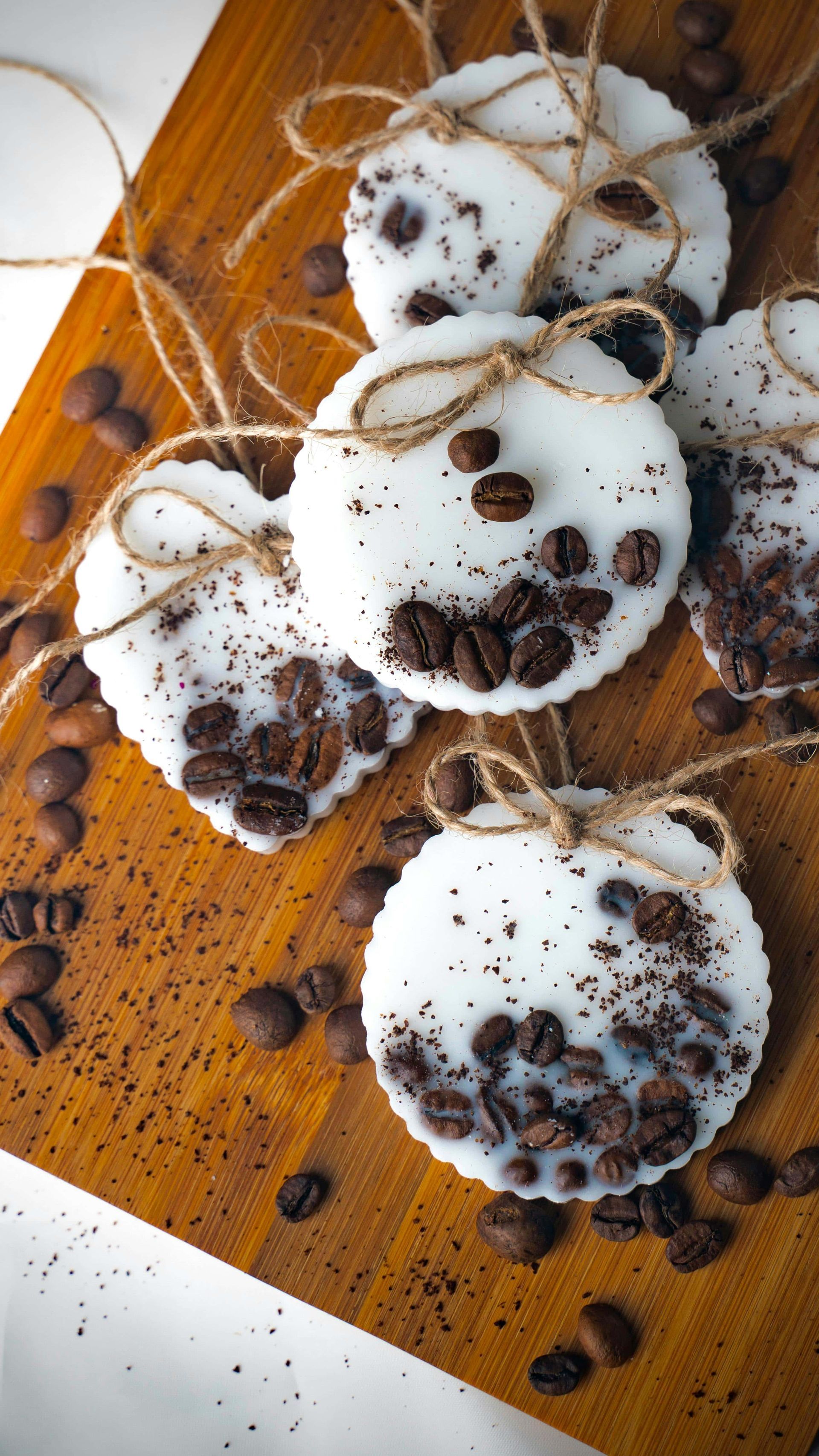 White, circular scented wax melts decorated with coffee beans and grounds on a wooden board, tied with twine.
