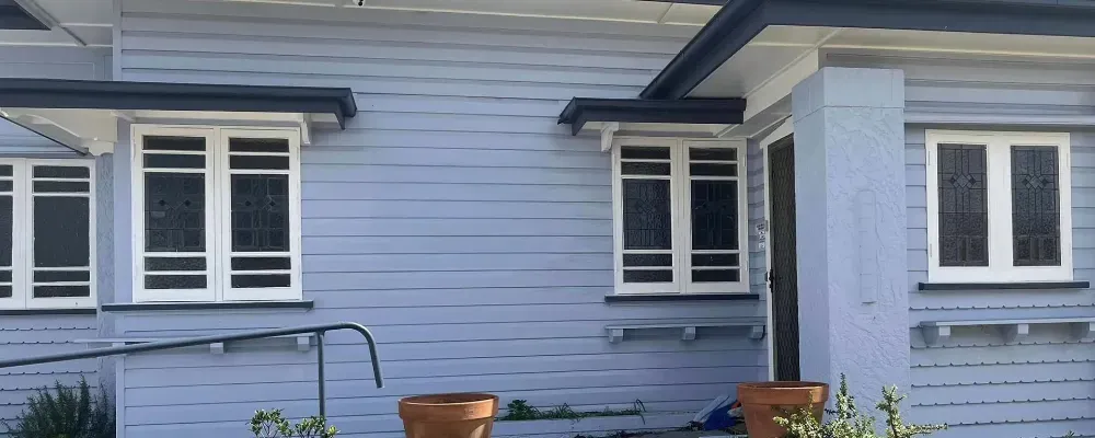 A blue house with white windows and potted plants in front of it.