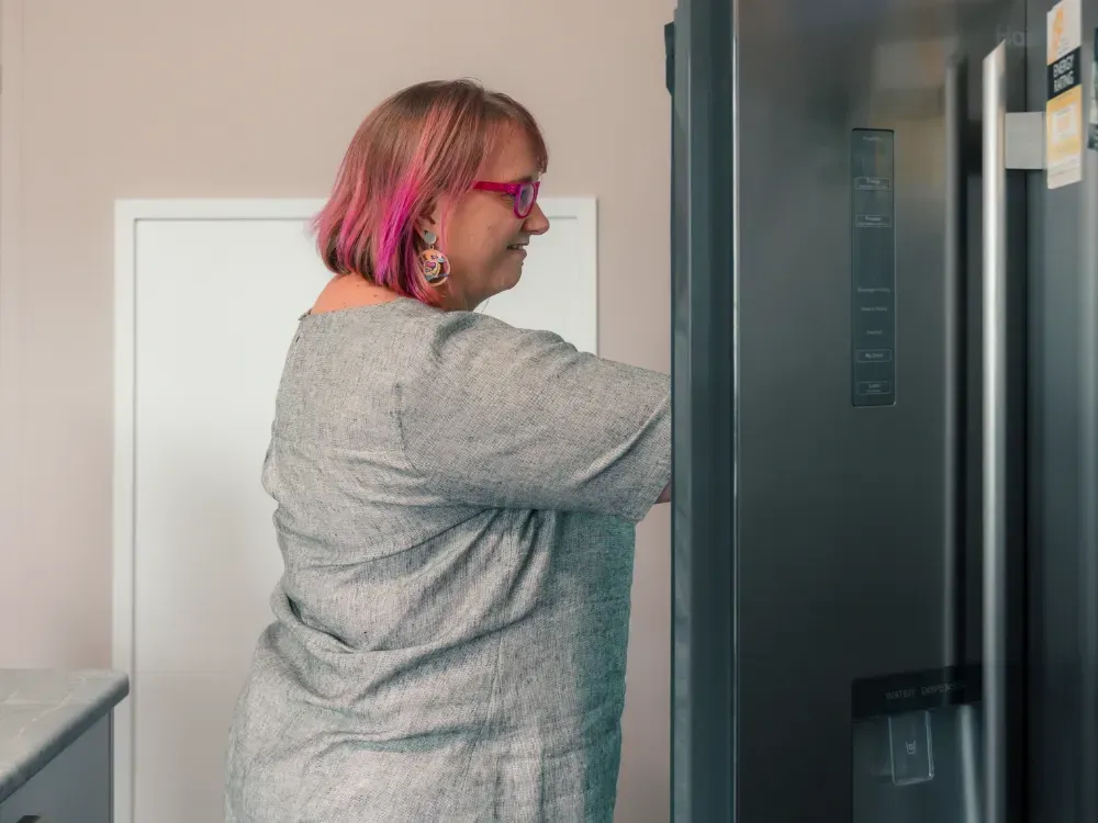 A woman with pink hair is opening a refrigerator door.