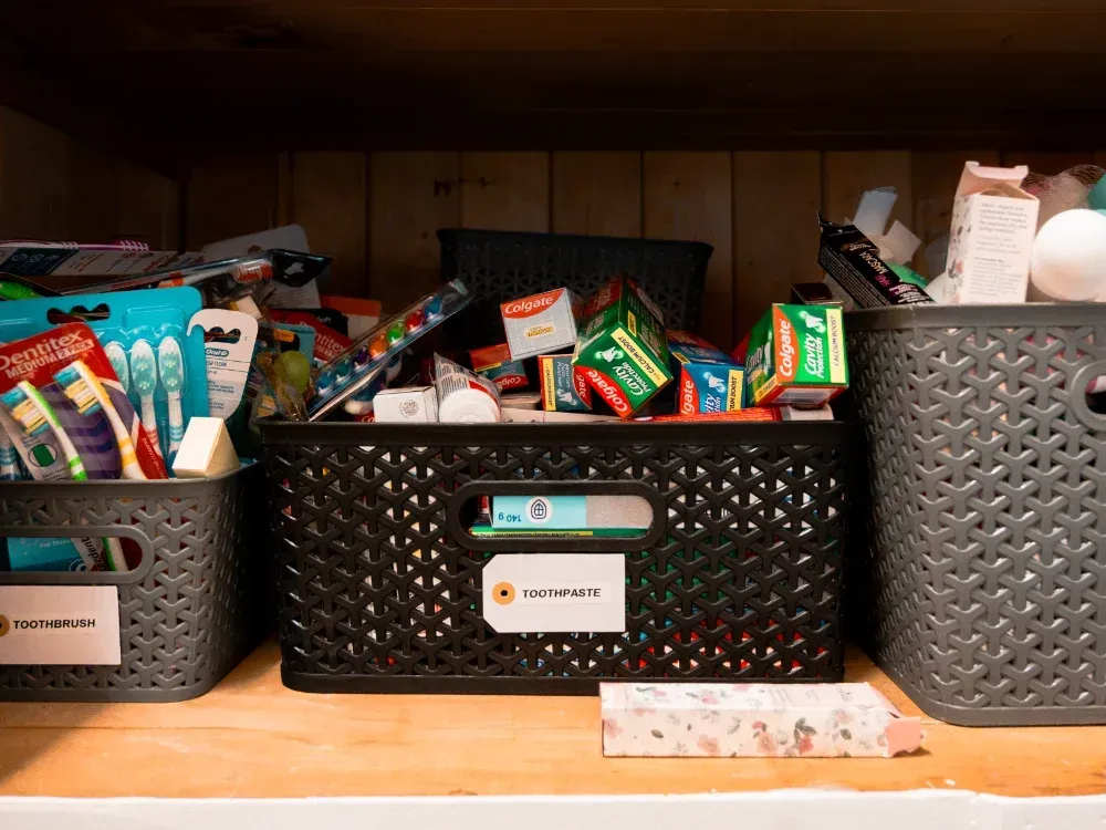 A shelf with three baskets filled with toothbrushes , toothpaste , and other items.