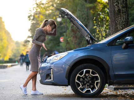 A woman is looking under the hood of her broken down car.