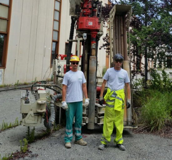 Due operai con indumenti protettivi sono in piedi accanto a una piattaforma di perforazione all'aperto in un cantiere edile.