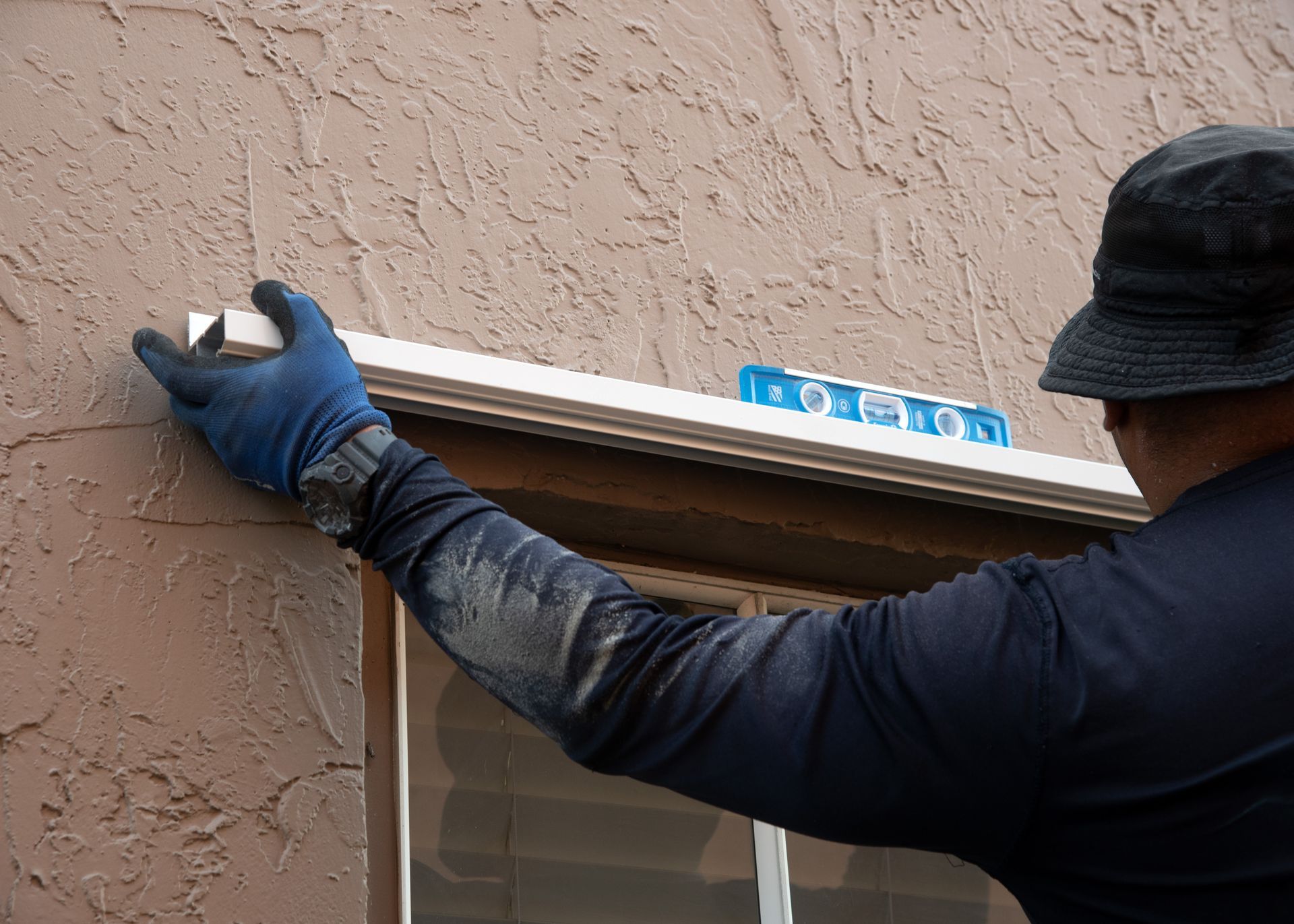  Installer using a level to mount hurricane shutter tracks on a stucco home window.]