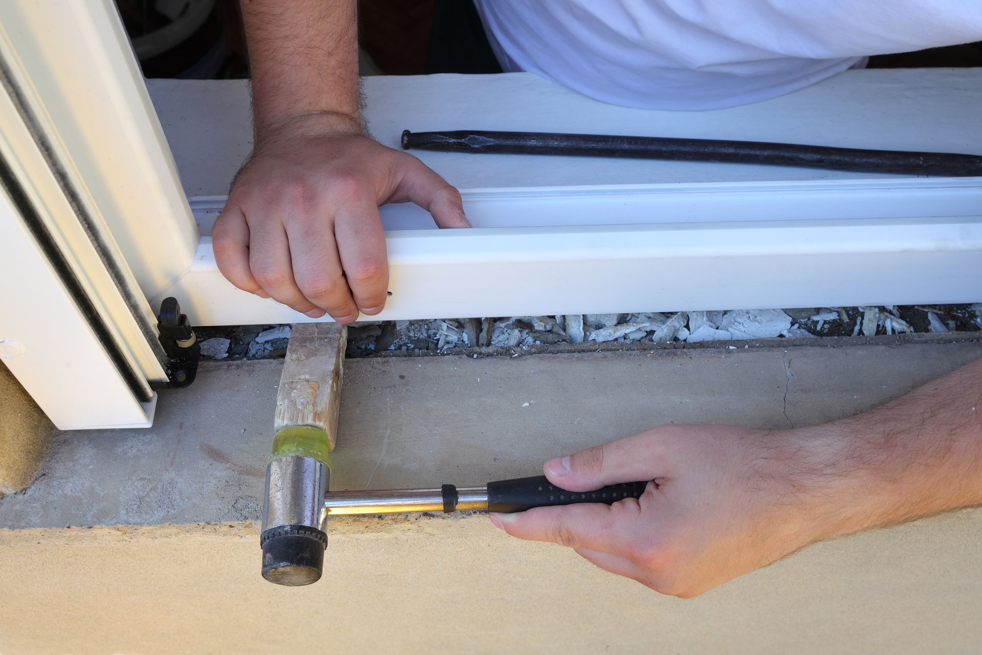 Installer using a hammer to fit a rubber seal into a window frame.