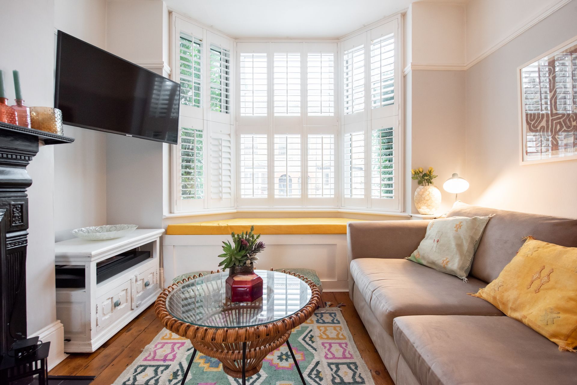 Bright living room with a large bay window featuring white plantation shutters.