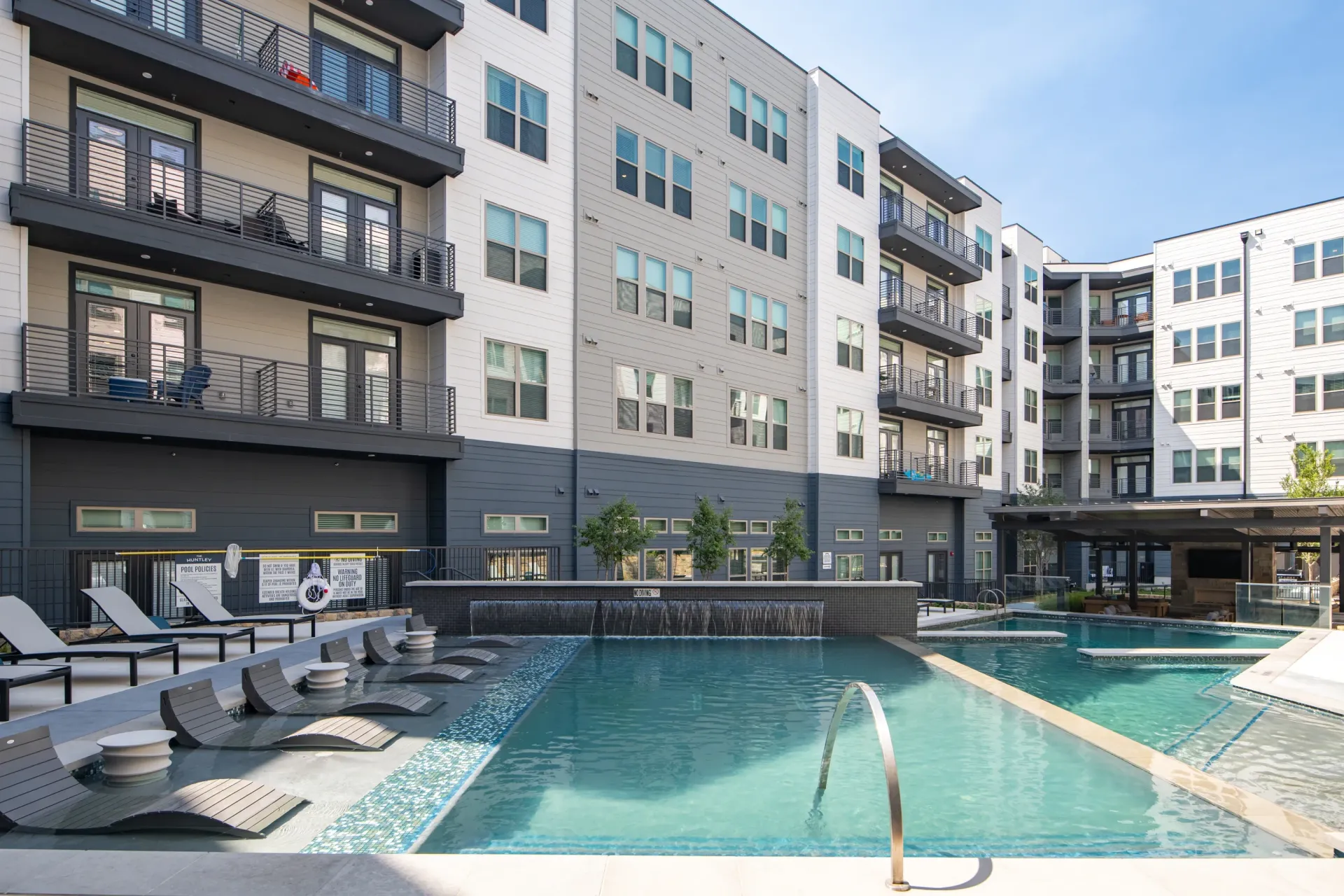 Luxury apartment building with a resort-style pool and lounge chairs.