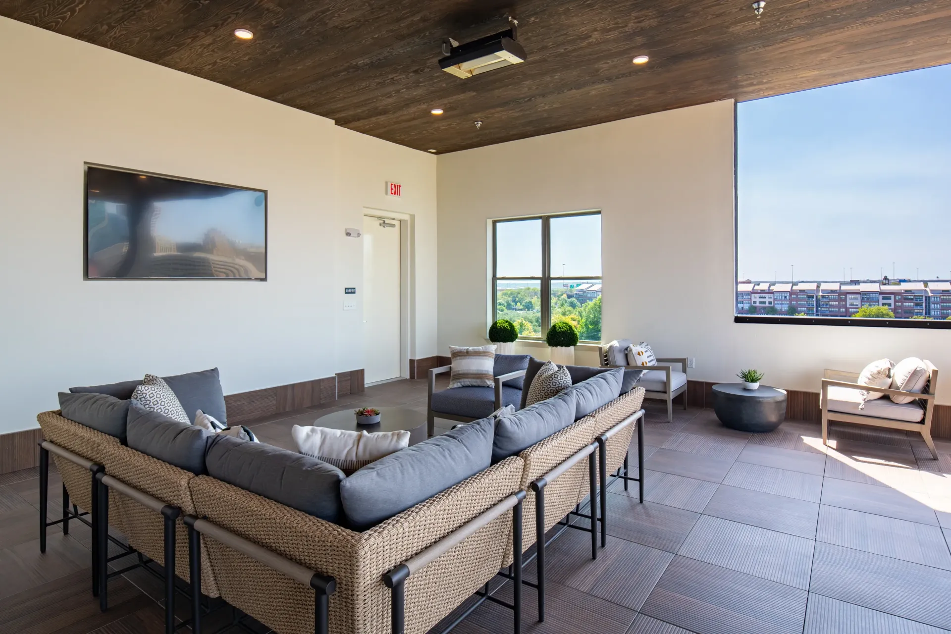 Rooftop lounge area with sectional sofa, chairs, coffee table, TV, and view of city buildings.