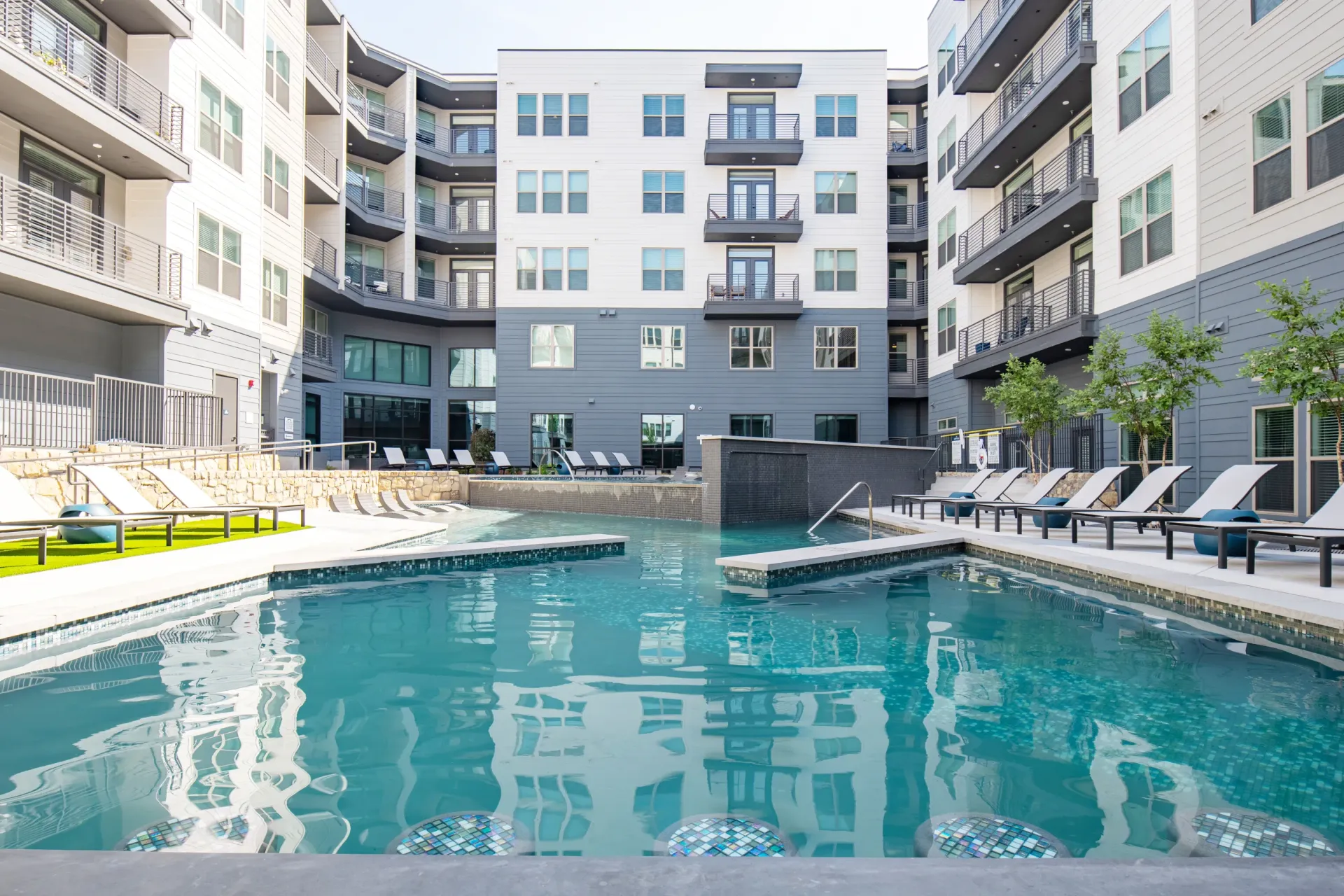 Modern apartment complex courtyard with a shimmering blue pool and lounge chairs.