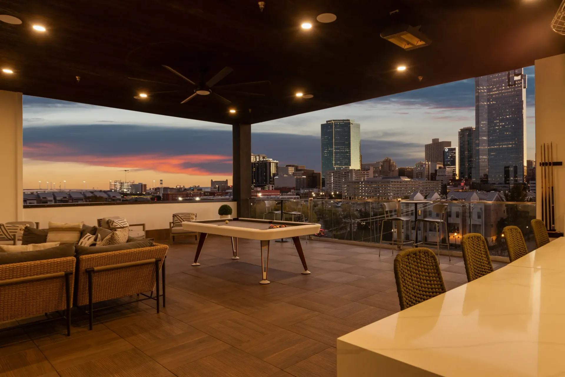 Rooftop lounge area with pool table and city skyline view at sunset.
