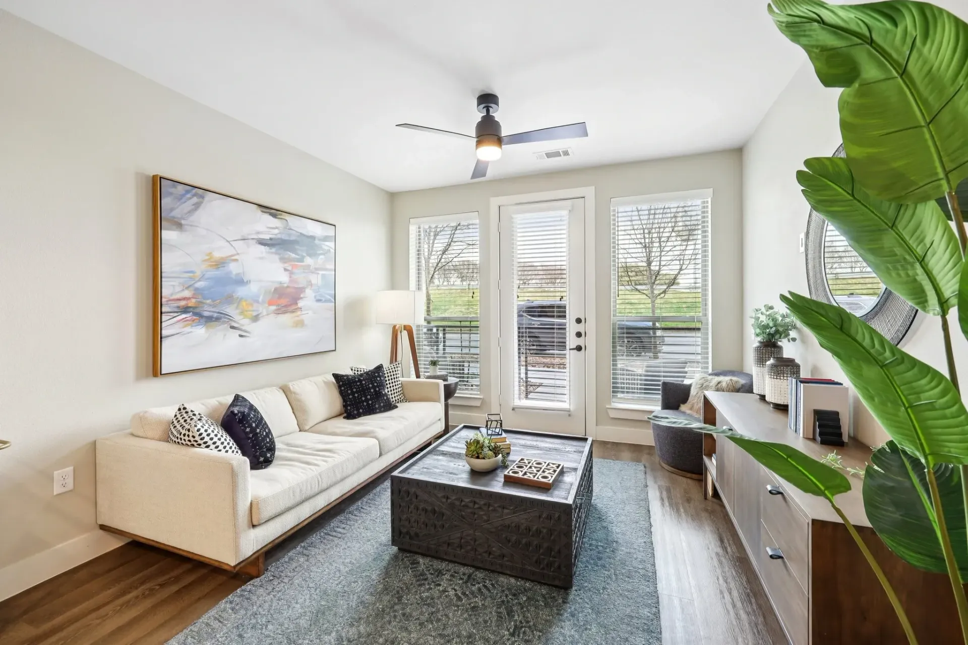 Modern living room with a cream sectional sofa, abstract art, and large windows.
