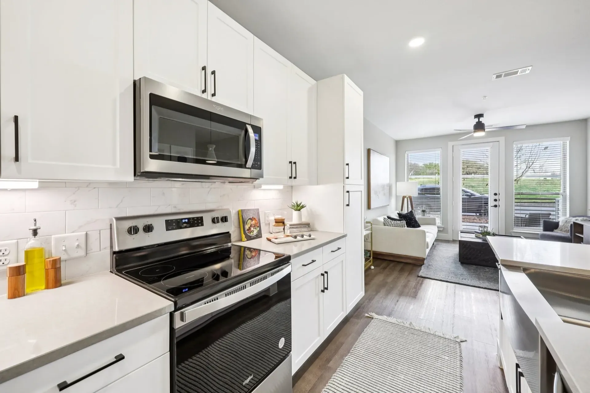 Modern kitchen with white cabinets and stainless steel appliances, open to living area.