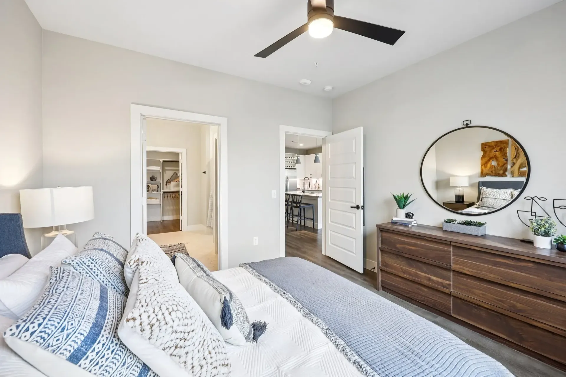 Cozy bedroom with a king-size bed, featuring a ceiling fan, large dresser, and a view into a walk-in closet and kitchen.