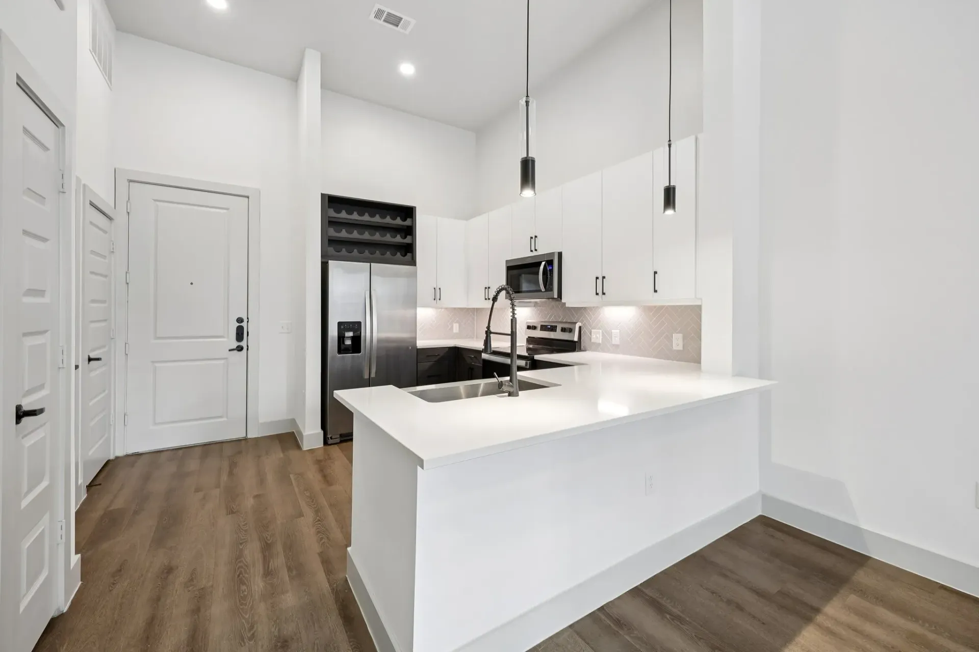 Modern kitchen with stainless steel appliances, white countertops, and pendant lighting.