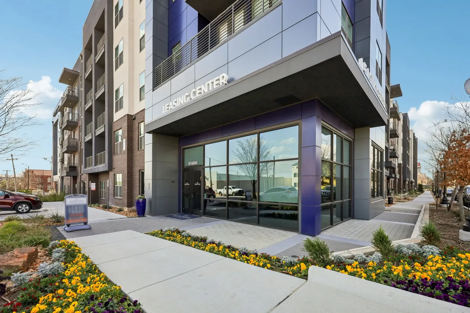 Exterior of the leasing center of a modern apartment building, with a sidewalk and landscaping in the foreground.