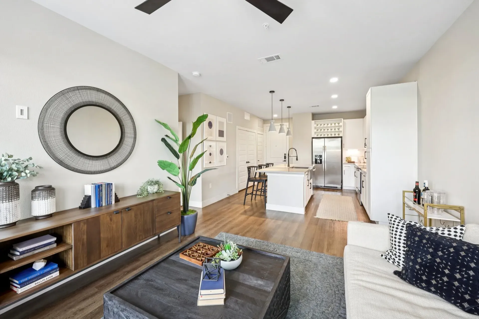 Living room and kitchen of an apartment with a modern design, featuring a large mirror and island.