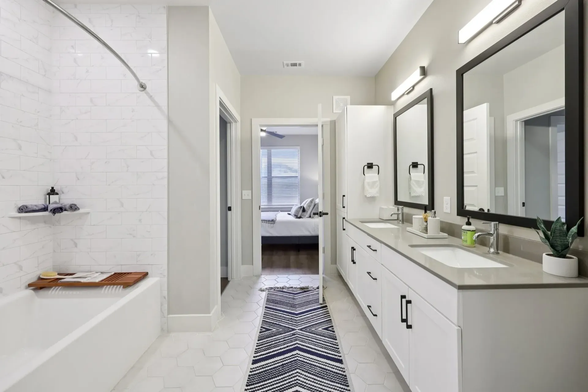 Modern bathroom with double vanity, bathtub, and view into bedroom.