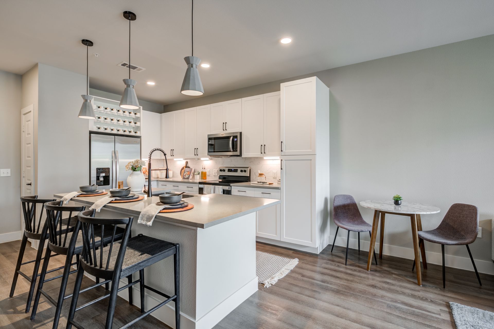 Modern kitchen and dining area with island, pendant lights, white cabinets, and two chairs by a small table