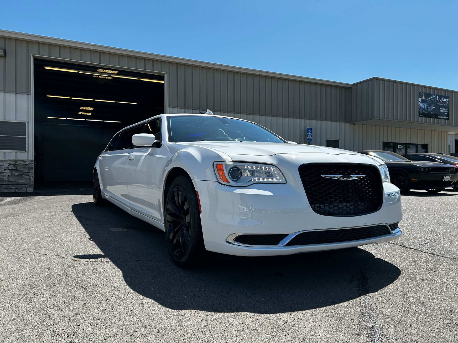 White Chrysler 300 sedan parked in front of a garage, sunny day.