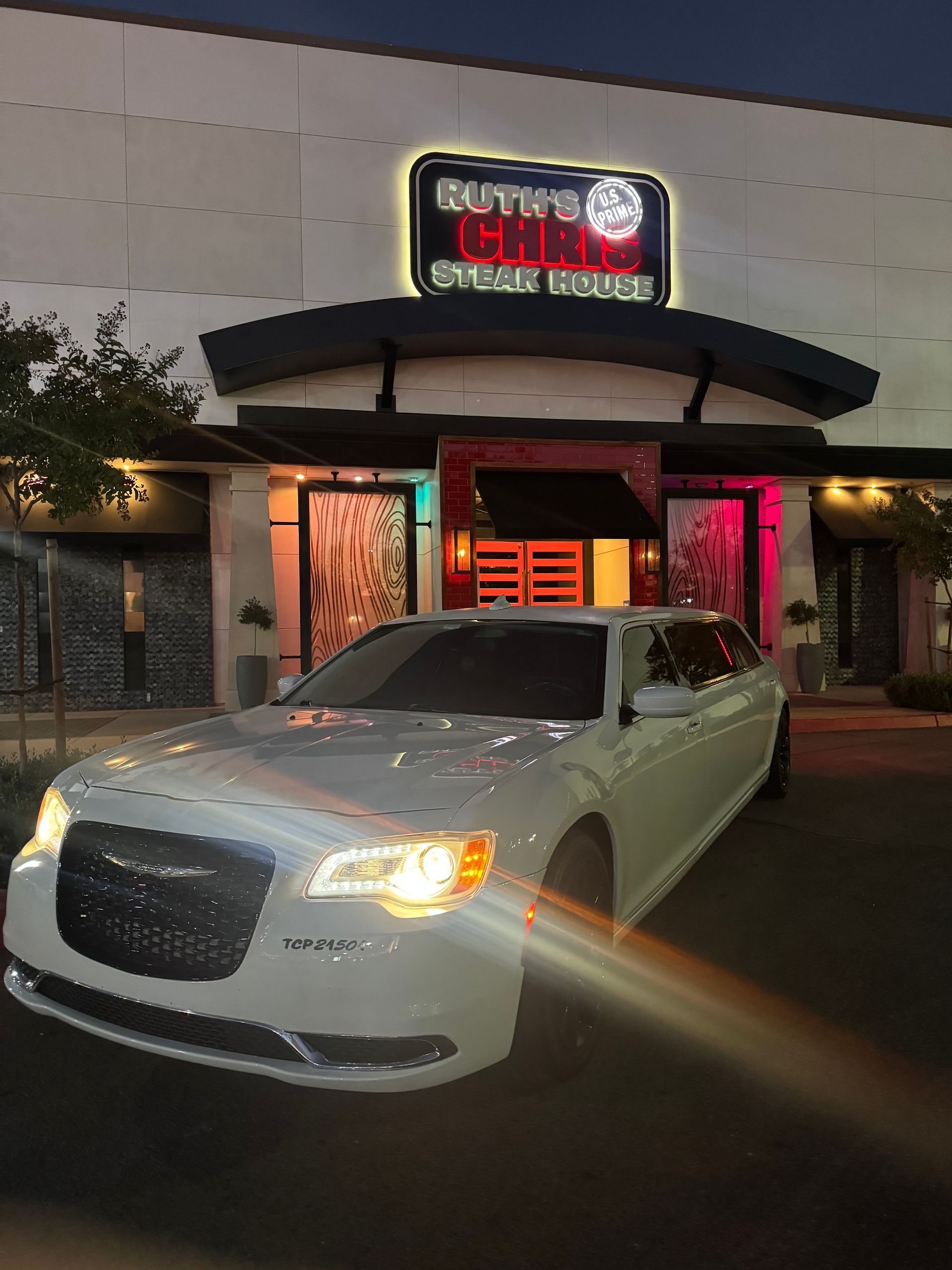 White car parked in front of Ruth's Chris Steak House with a lit-up sign.