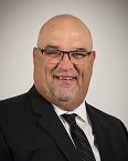 Bald man in glasses and suit smiles, white background.