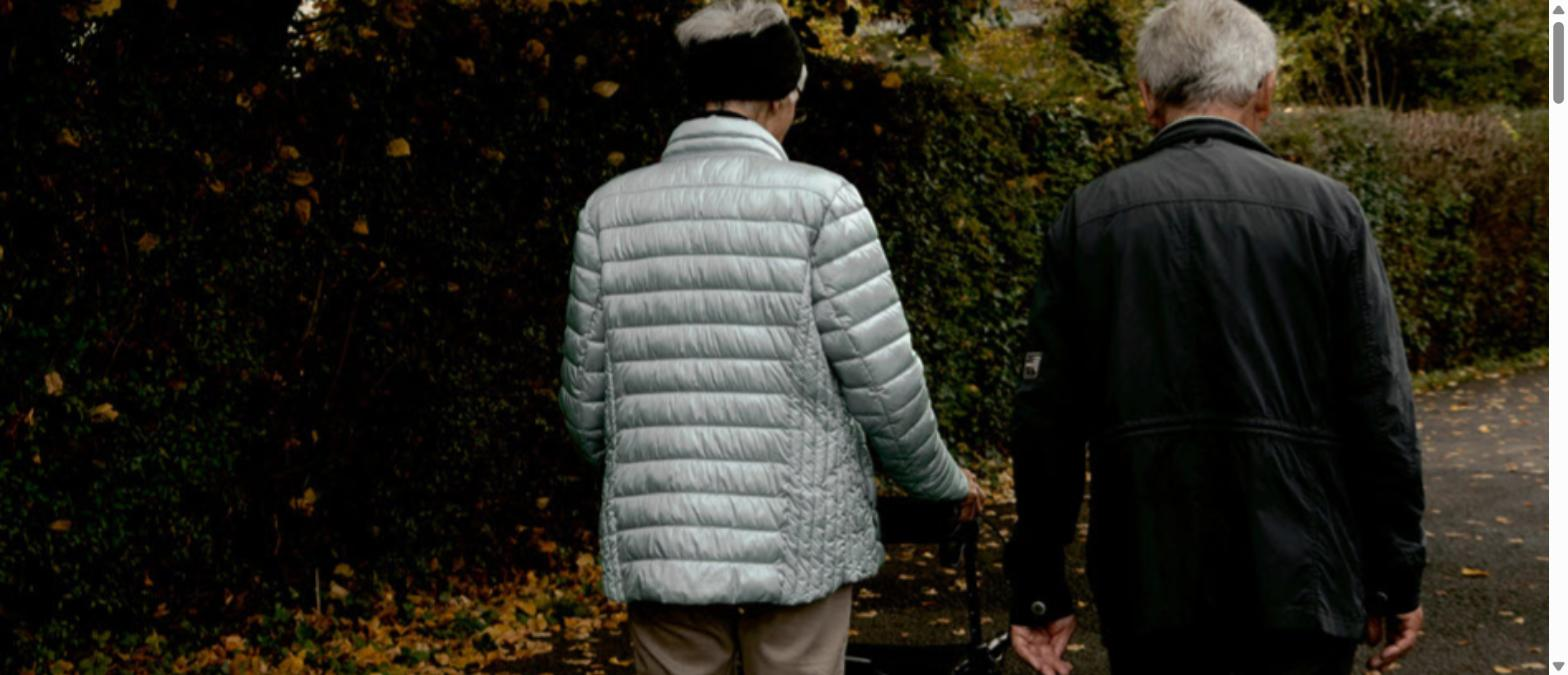 Elderly couple walking together outdoors on an autumn path, seen from behind