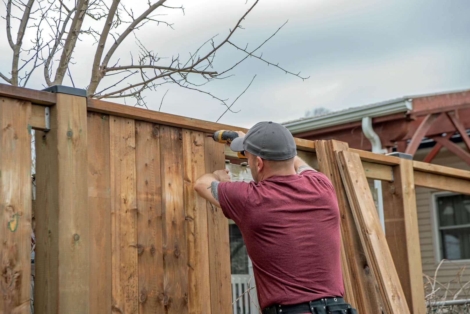 A man is fixing a wooden fence with a drill.