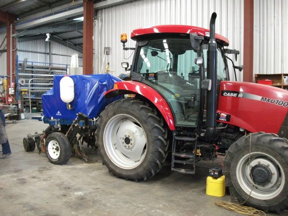 Red Case IH tractor pulling a blue planter in a workshop.